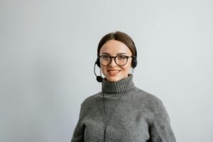 Smiling female call center agent wearing headphones and a gray sweater, ready to assist.