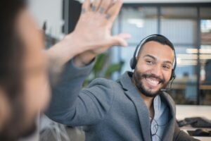 A cheerful call center agent with a headset gives a high five to a colleague in an office.